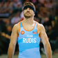 A focused male wrestler in a blue singlet representing Team Rudis wearing a black headband and displaying determination before a match