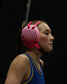Person wearing a blue wrestling singlet and pink headgear against a black background