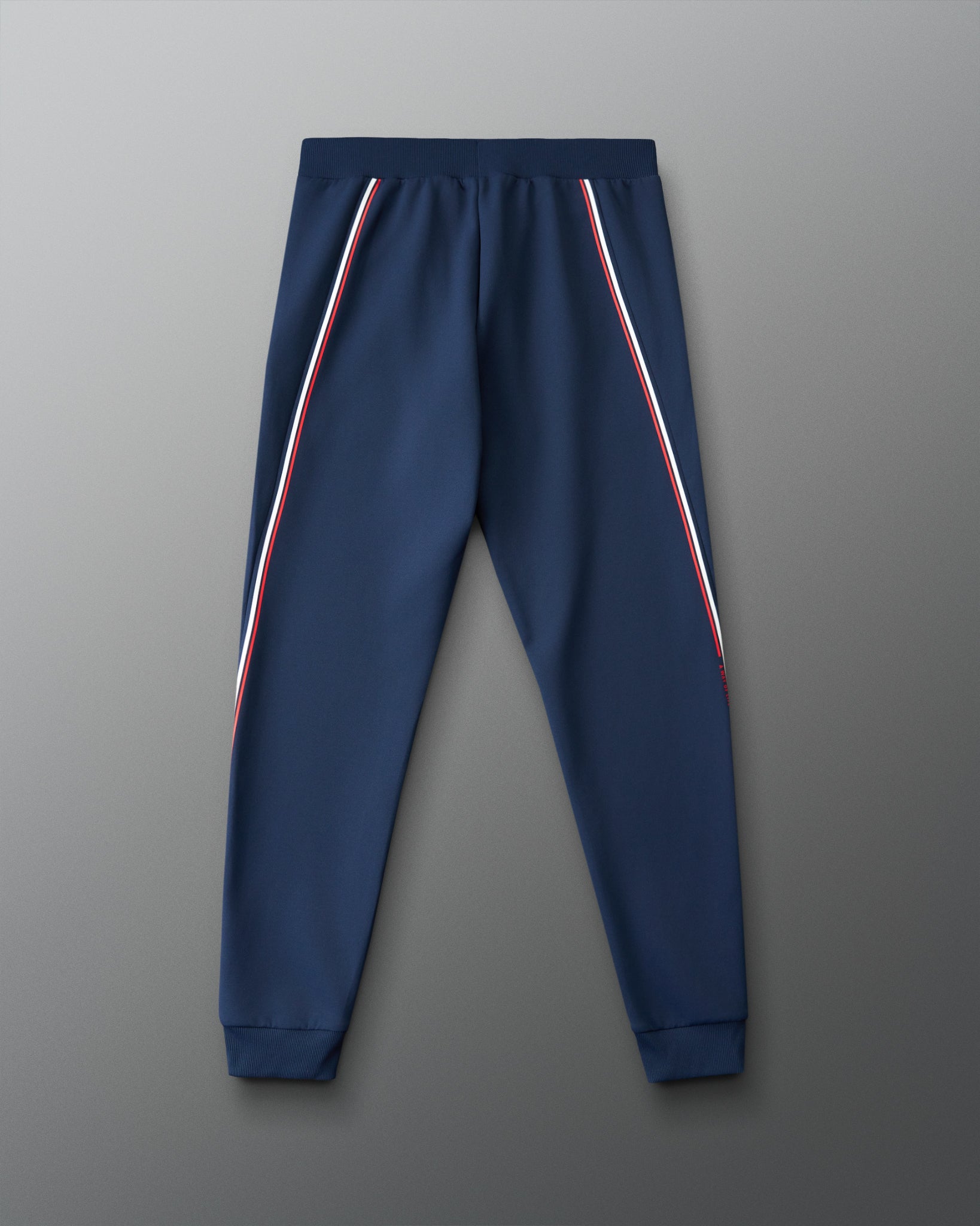 Navy blue jogger pants with red and white stripes on a gray background