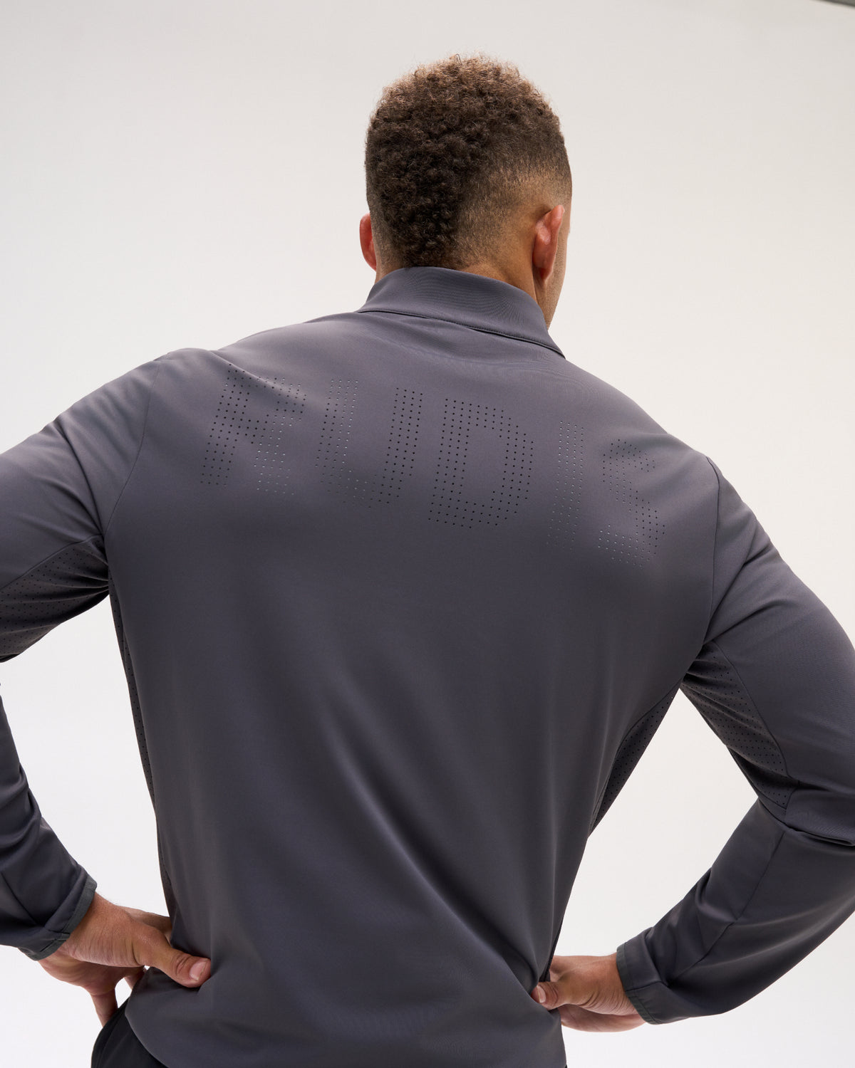 Back view of the carbon RUDIS Victory 1/4 Zip featuring perforated RUDIS lettering across the upper back and ventilated panels.