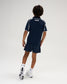Back view of a youth model wearing the RUDIS Chronicle Elite Youth Athletic Polo in Navy, highlighting white RUDIS lettering below the collar, contrast piping along the shoulders, and short sleeves.
