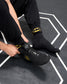 Wrestler wearing black RUDIS Batman Cushion Crew Socks with yellow Batman logos while putting on a black Batman wrestling shoe.