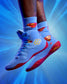 RUDIS JB1 Superman wrestling shoes worn with matching Superman socks against a comic-inspired blue and pink background.