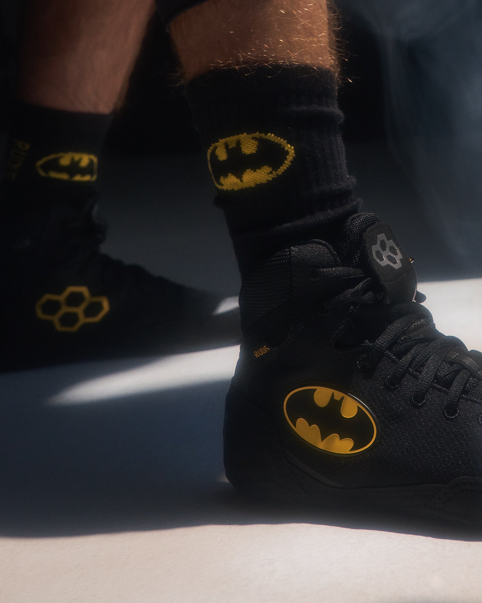 Athlete wearing RUDIS x Batman Colt 4.0 adult wrestling shoes in black with the iconic yellow Batman logo, paired with matching Batman crew socks featuring the classic bat emblem.