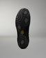 The black textured sole of a wrestling shoe, shown from a top-down view against a neutral gray background. The sole features a honeycomb-like tread pattern and a small yellow logo in the center.