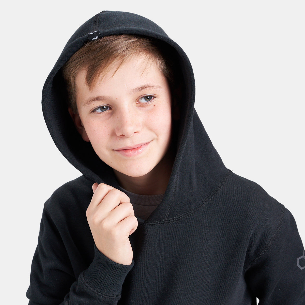 A young boy smiles while wearing a black hoodie looking casual and relaxed against a light gray background