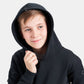 A young boy smiles while wearing a black hoodie looking casual and relaxed against a light gray background