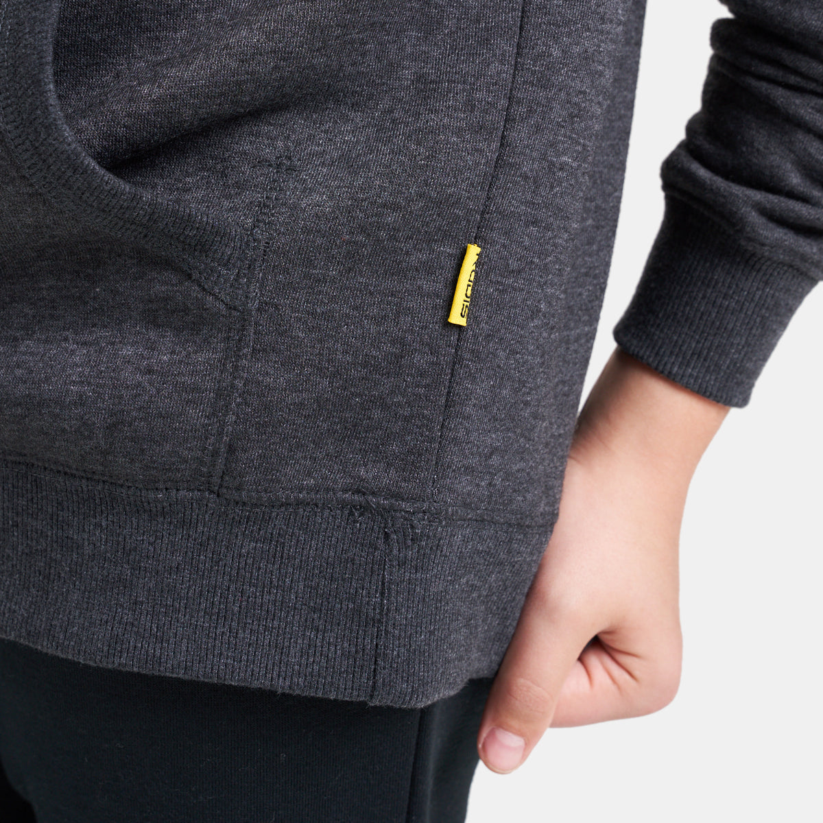 A close-up view of a gray hoodie pocket and sleeve featuring a small brand tag in yellow indicative of casual wear