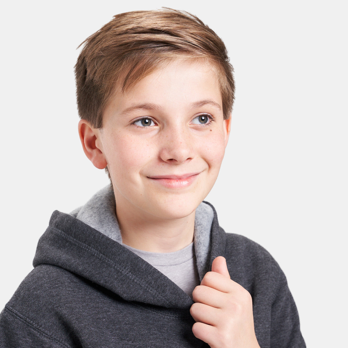 A young boy with short brown hair and blue eyes smiles while wearing a dark hoodie over a gray shirt capturing a moment of warmth and friendliness