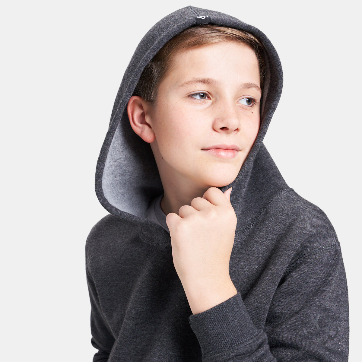 A young boy wearing a gray hoodie with a cozy interior looking thoughtfully to the side with a gentle smile