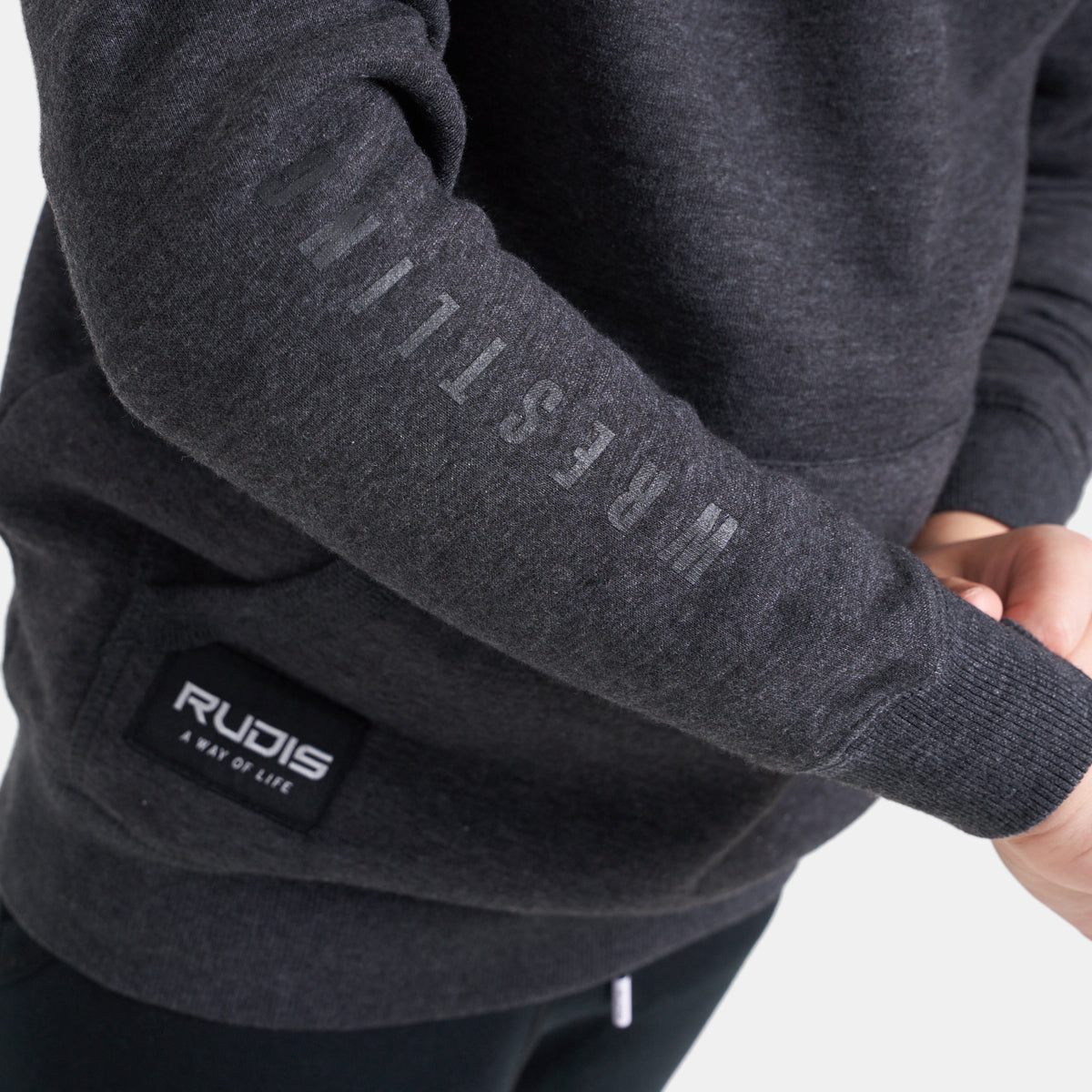 A close-up view of a dark gray sweatshirt featuring the word WRESTLING printed along the sleeve and the brand logo RUDIS displayed on a patch at the bottom left