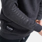 A close-up view of a dark gray sweatshirt featuring the word WRESTLING printed along the sleeve and the brand logo RUDIS displayed on a patch at the bottom left