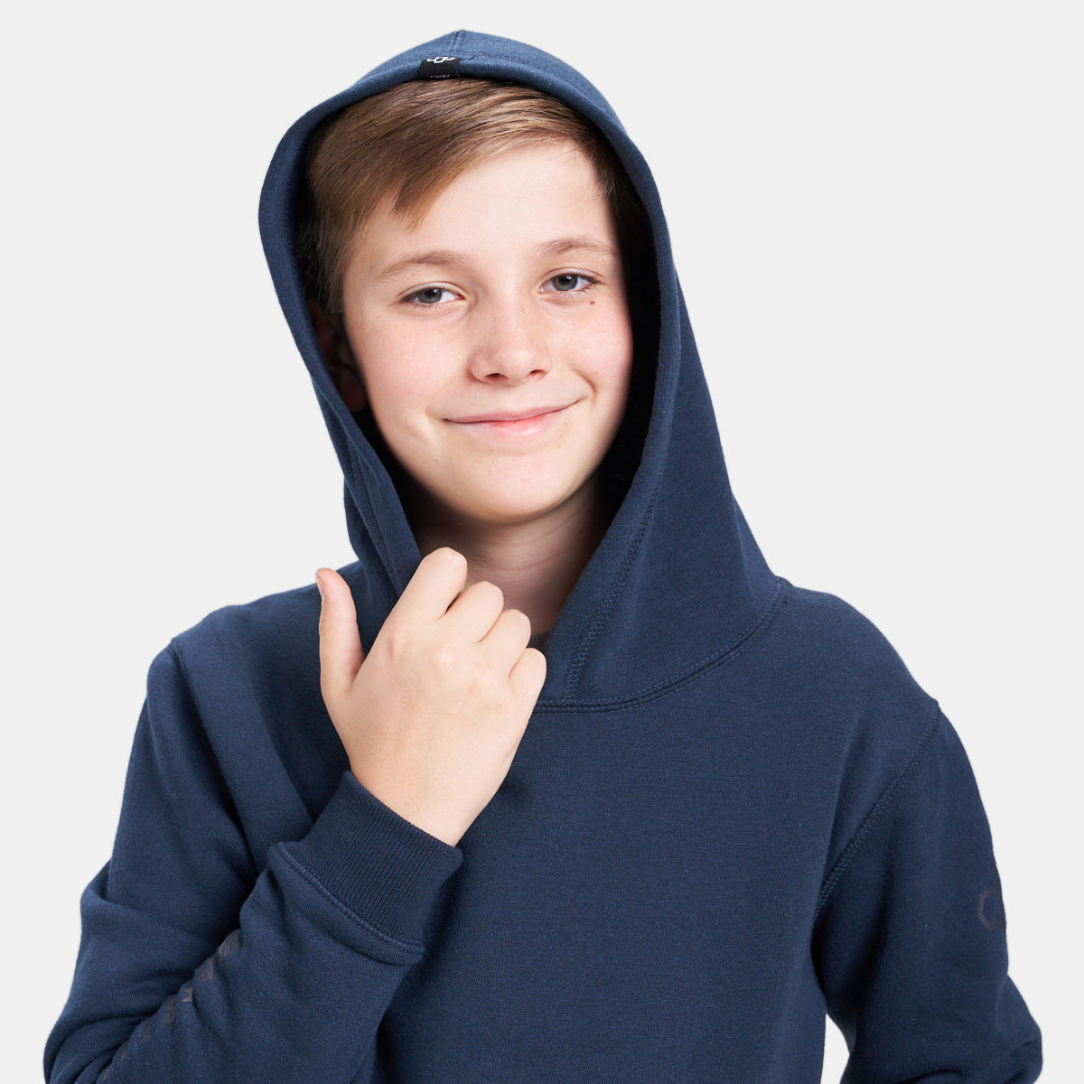 A young boy smiles while wearing a navy blue hooded sweatshirt gently holding the fabric near his chin