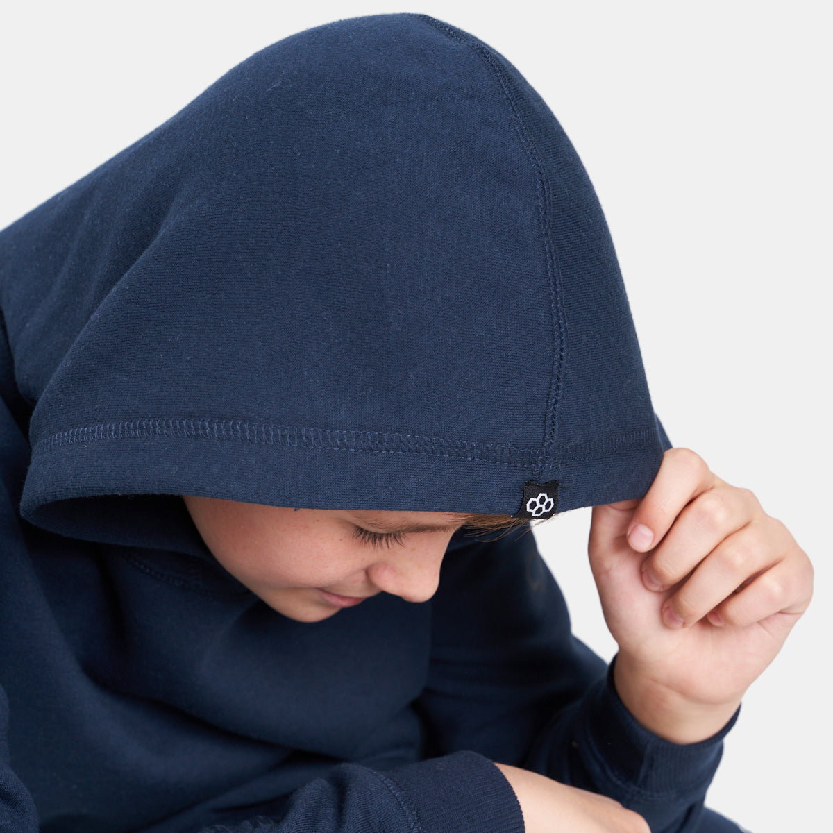 A close-up of a child wearing a navy blue hoodie with a hood drawn over their head looking down with a thoughtful expression