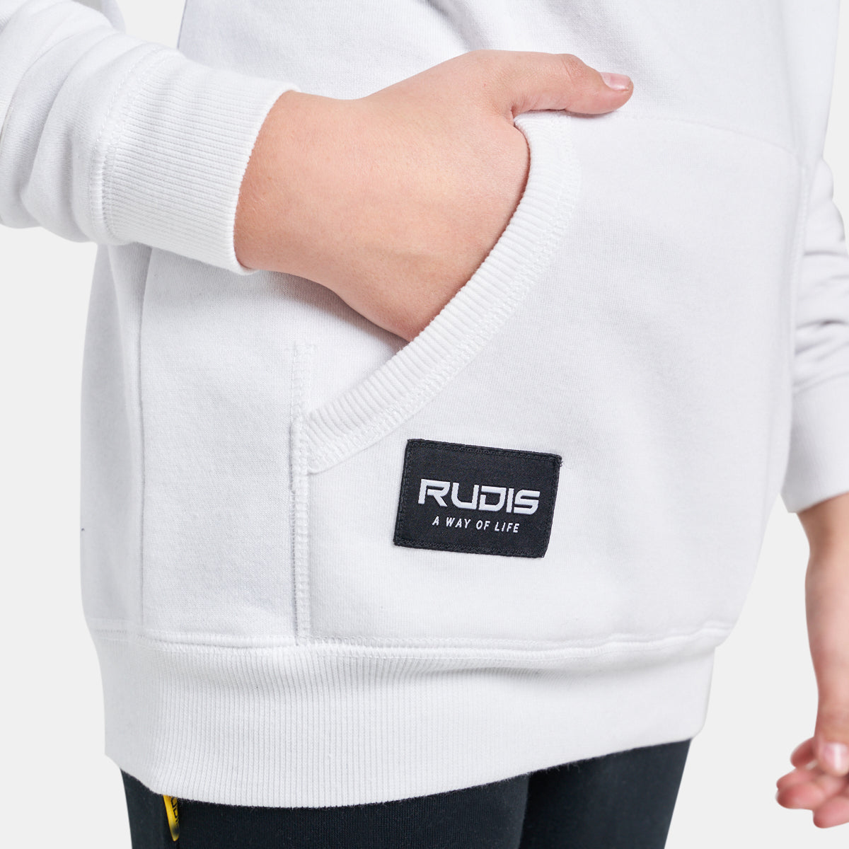 A close-up view of a person wearing a white hoodie featuring a front pocket and a branded tag that reads RUDIS A WAY OF LIFE