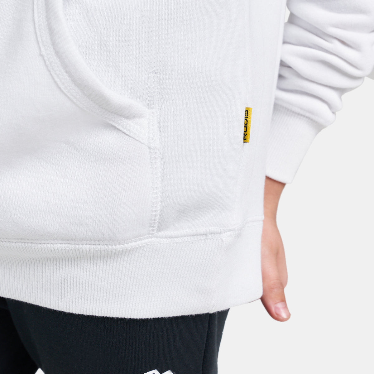 A close-up of a white hoodie featuring a kangaroo pocket and a branded label complemented by black leggings