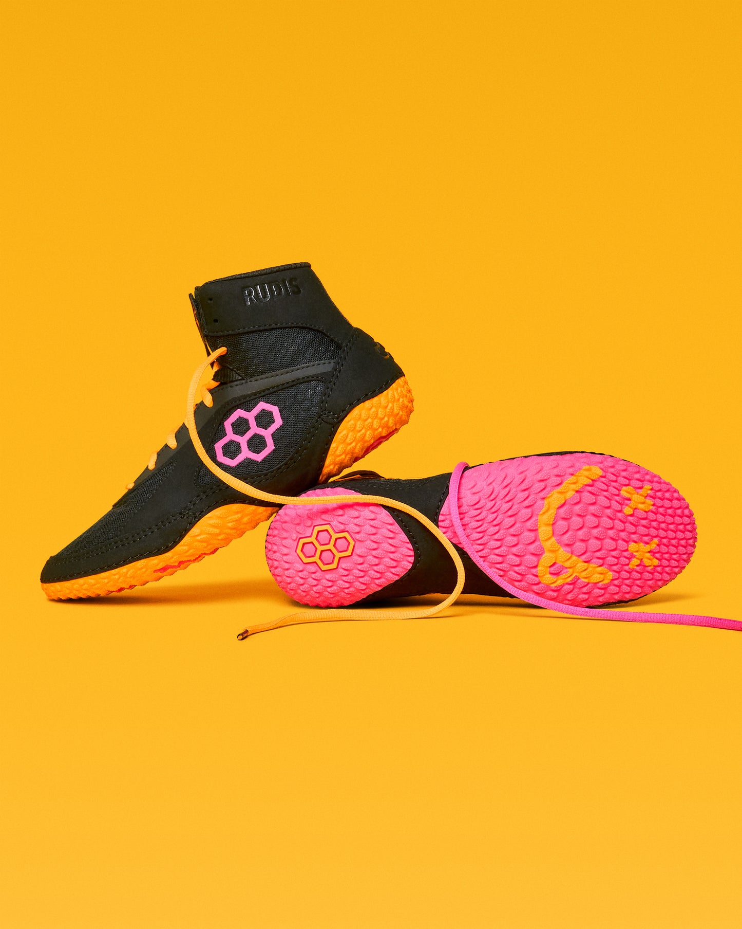 Black and pink wrestling shoes with yellow accents on a yellow background