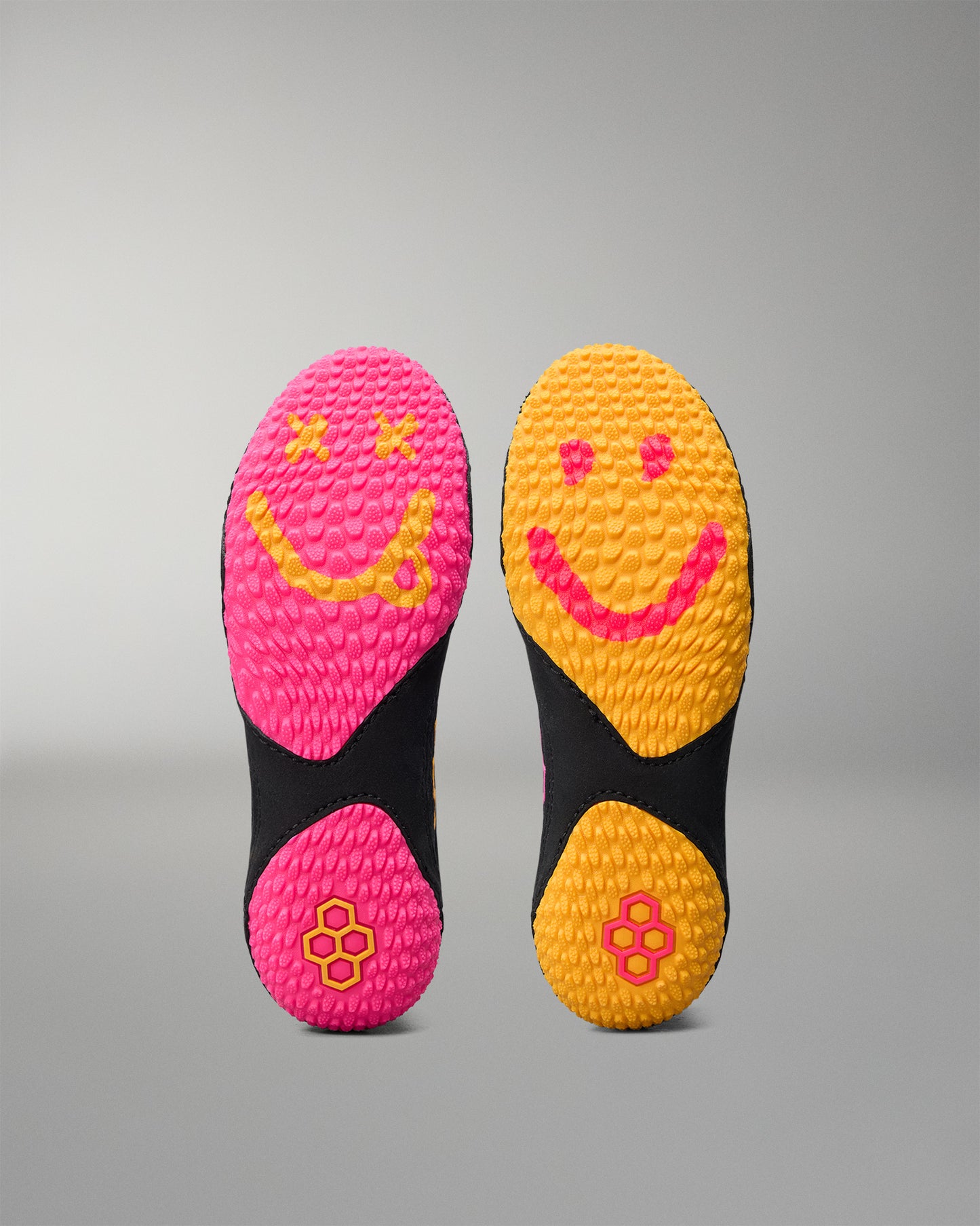 Two pairs of colorful wrestling shoe soles with smiley face designs on a gray background