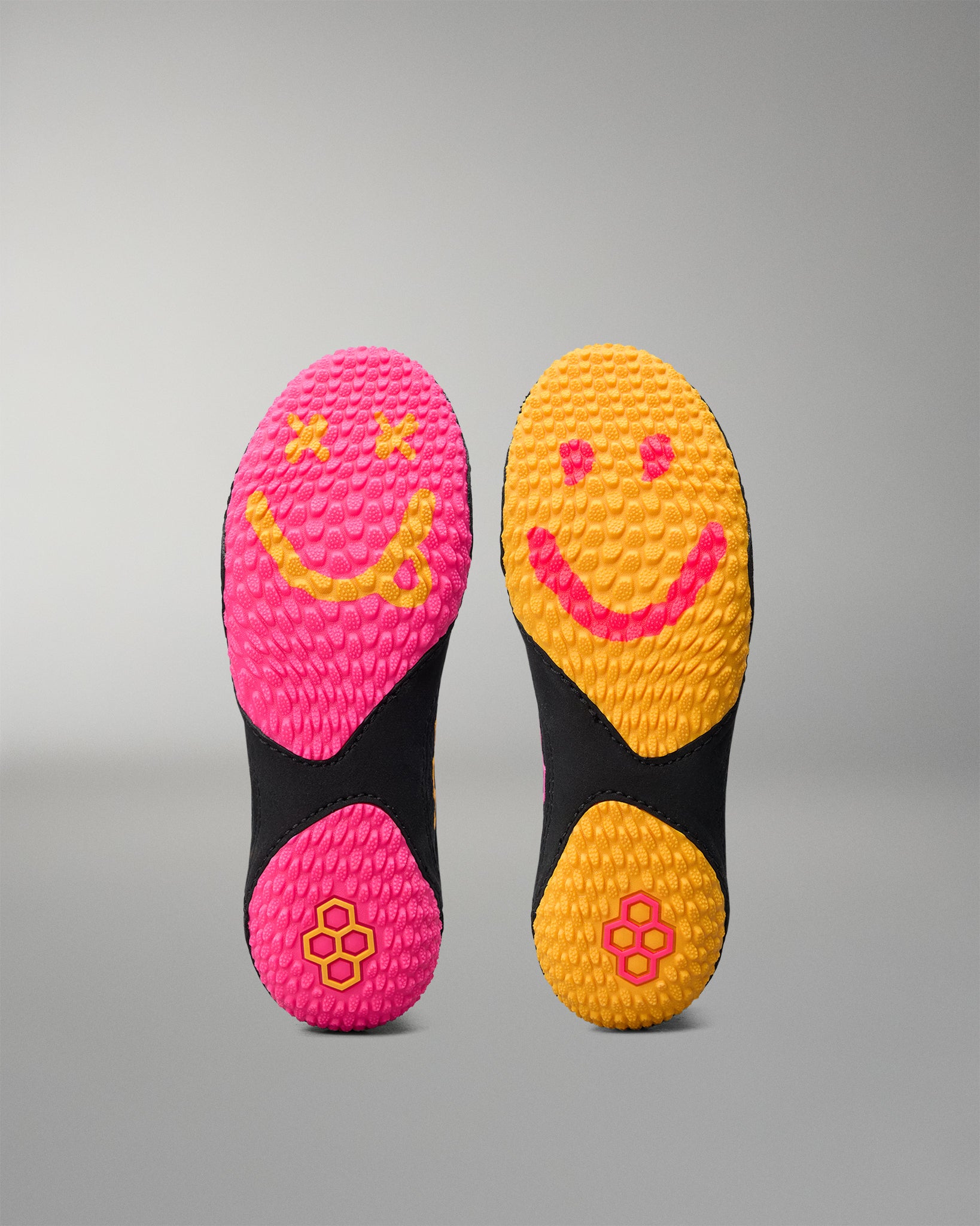 Two pairs of colorful wrestling shoe soles with smiley face designs on a gray background