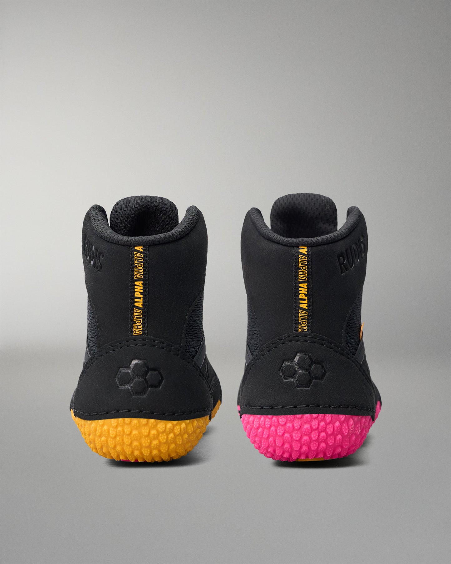Black wrestling shoes with yellow and pink soles on a gray background