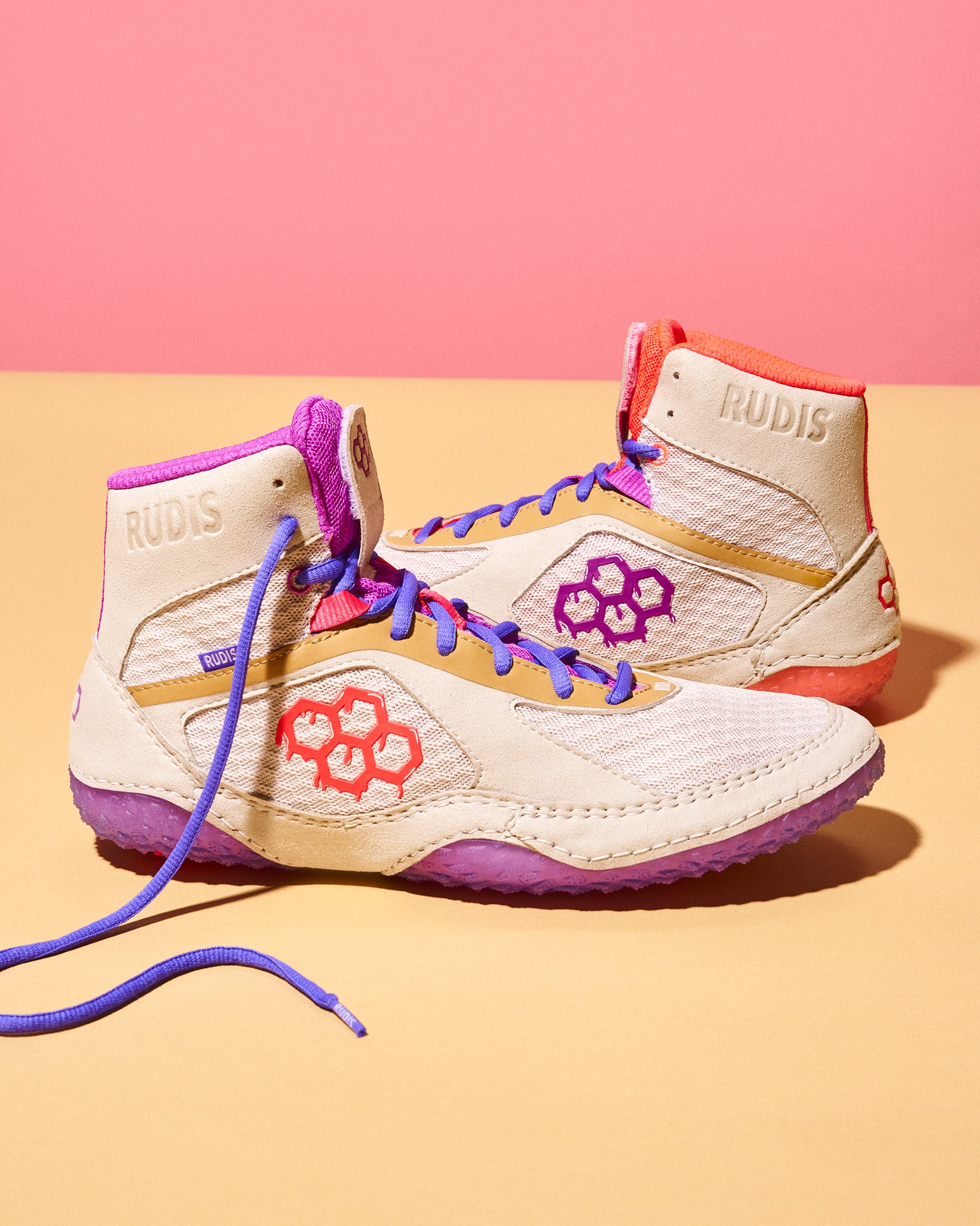 Colorful wrestling shoes with brand logo on a pink and beige background