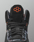 Black wrestling shoe with orange logo on a gray background