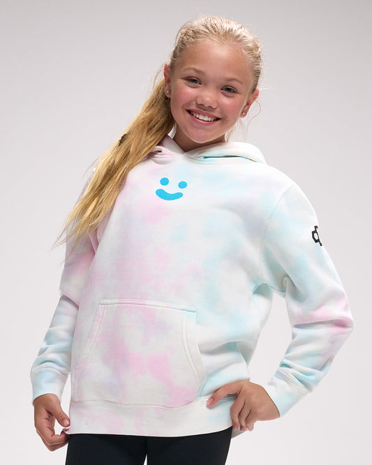 Young girl wearing a tie-dye hoodie with a smiley face design on a gray background