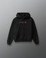 A black pullover hoodie with a small chest graphic featuring pink and white symbols, displayed against a dark gray gradient background.