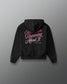 A black hoodie shown from the back, featuring the phrase 'I've Been Dreaming About It' printed in pink and white script across the upper back, displayed against a dark gray gradient background.