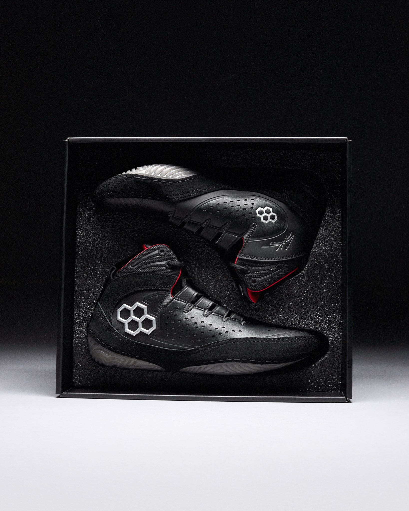 Black wrestling shoes with red accents in a black box on a dark background