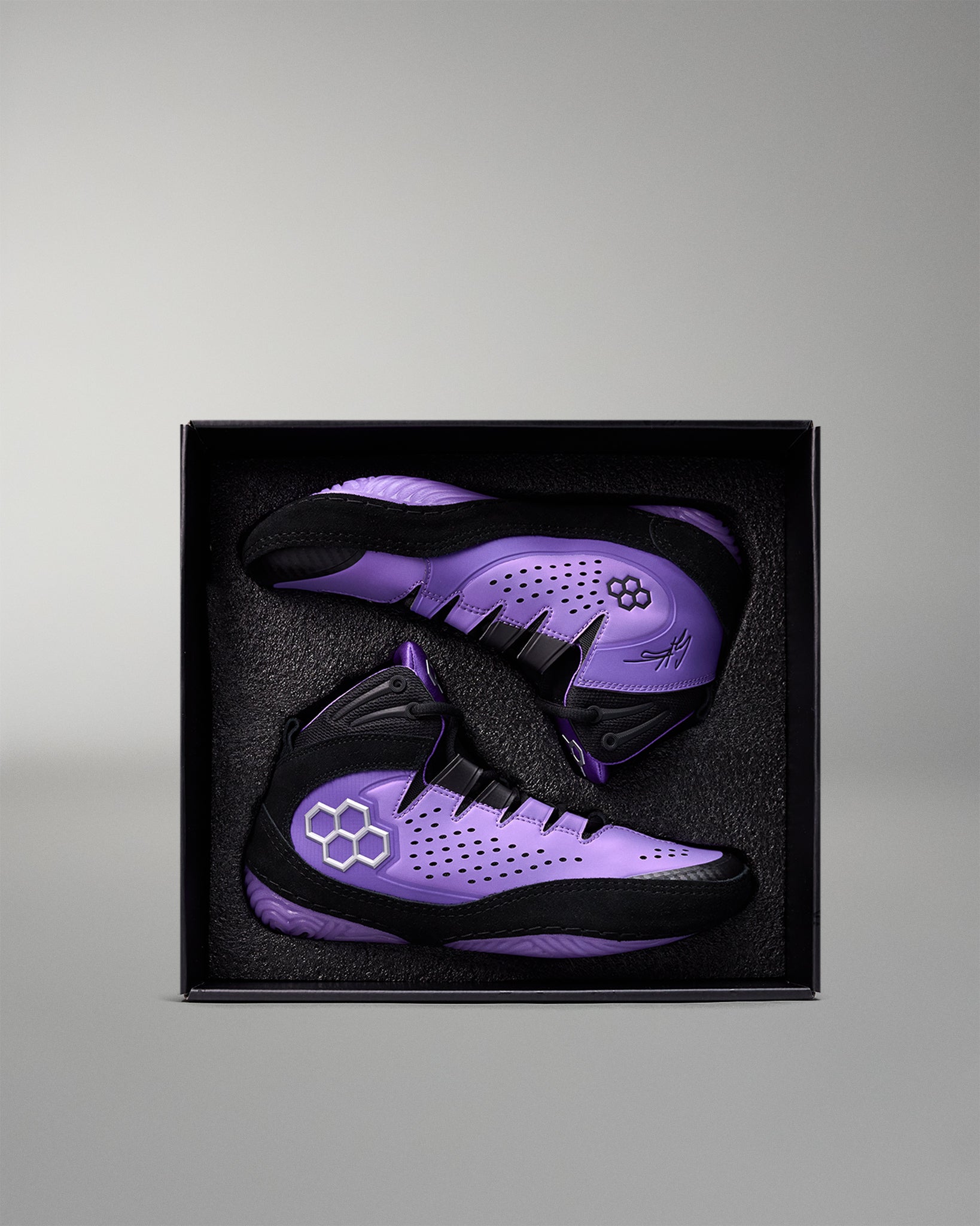 Purple and black wrestling shoes in a black box on a gray background