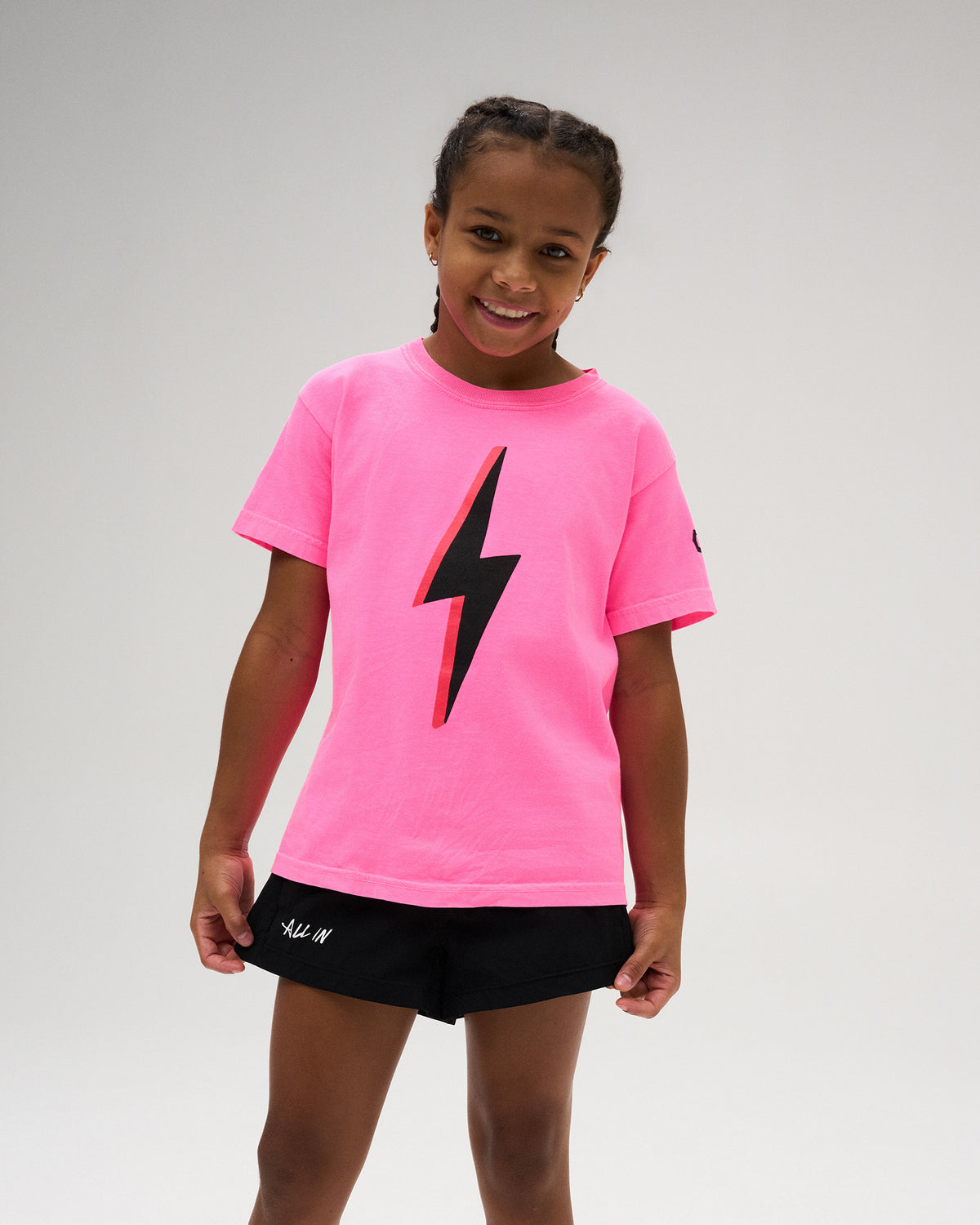 RUDIS Sarah Hildebrandt Bolt Neon Youth Heavyweight T-Shirt in Neon Pink, featuring a bold black lightning bolt chest graphic and RUDIS sleeve branding.