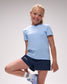 Young girl wearing a light blue sports outfit with a logo on a plain background