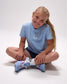 Young girl wearing a light blue t-shirt with a smiley face design, sitting on the floor with colorful socks.