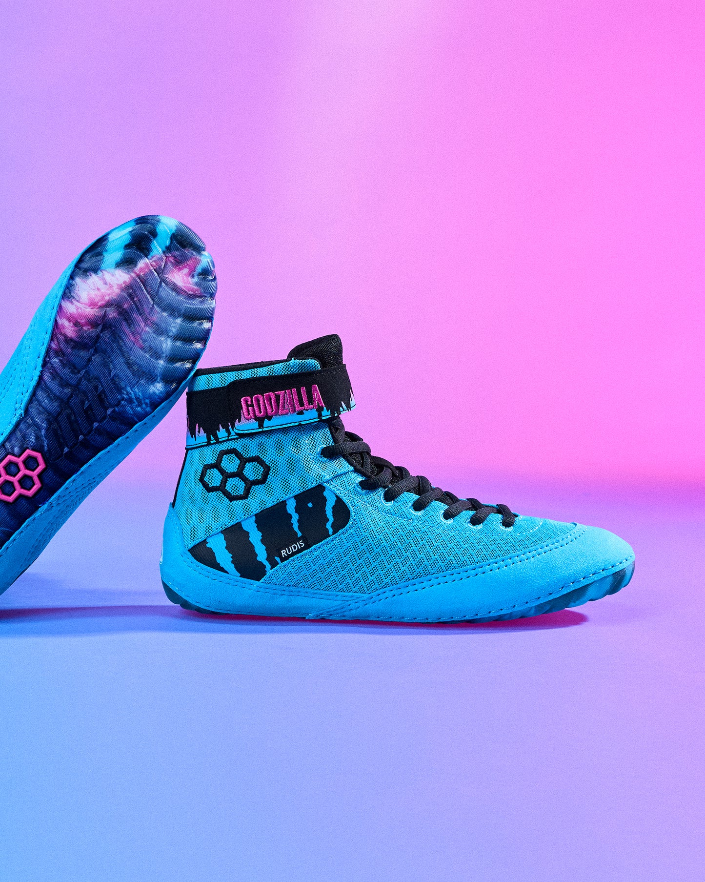 RUDIS Godzilla Samurai Speed Youth Wrestling Shoes in bright blue with black laces, Godzilla ankle strap, and graphic outsole displayed against a blue and pink gradient background.