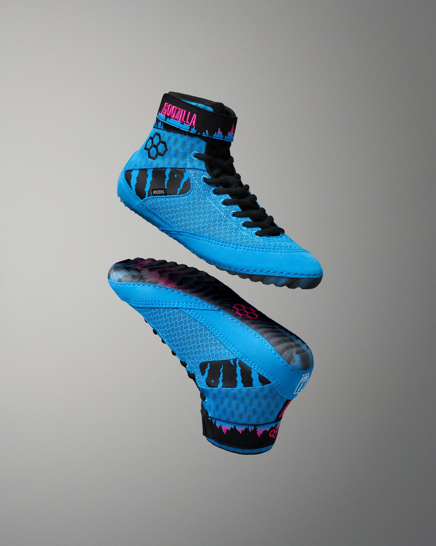Floating pair of RUDIS Godzilla Samurai Speed Youth Wrestling Shoes showcasing the side profile and colorful Godzilla-inspired outsole with bright blue upper and black accents.