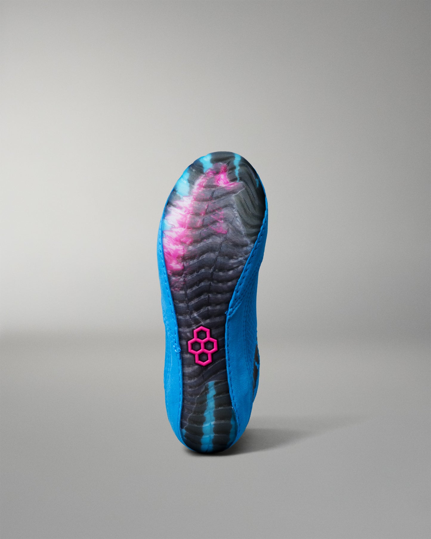 The outsole of a wrestling shoe is shown from the bottom, featuring a vibrant blue and black patterned design with a pink logo in the center.