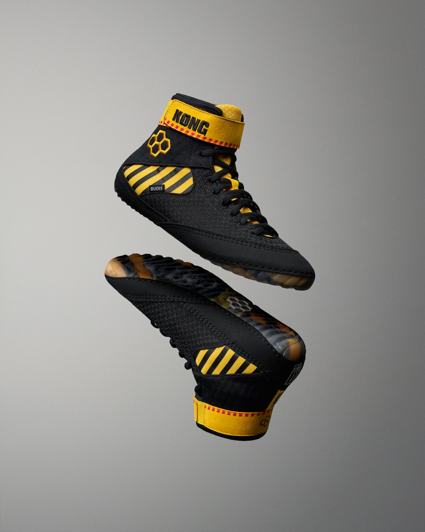 Black high-top wrestling shoes with bold yellow accents and the brand name KONG visible on the ankle strap, shown floating against a smooth gray gradient background.
