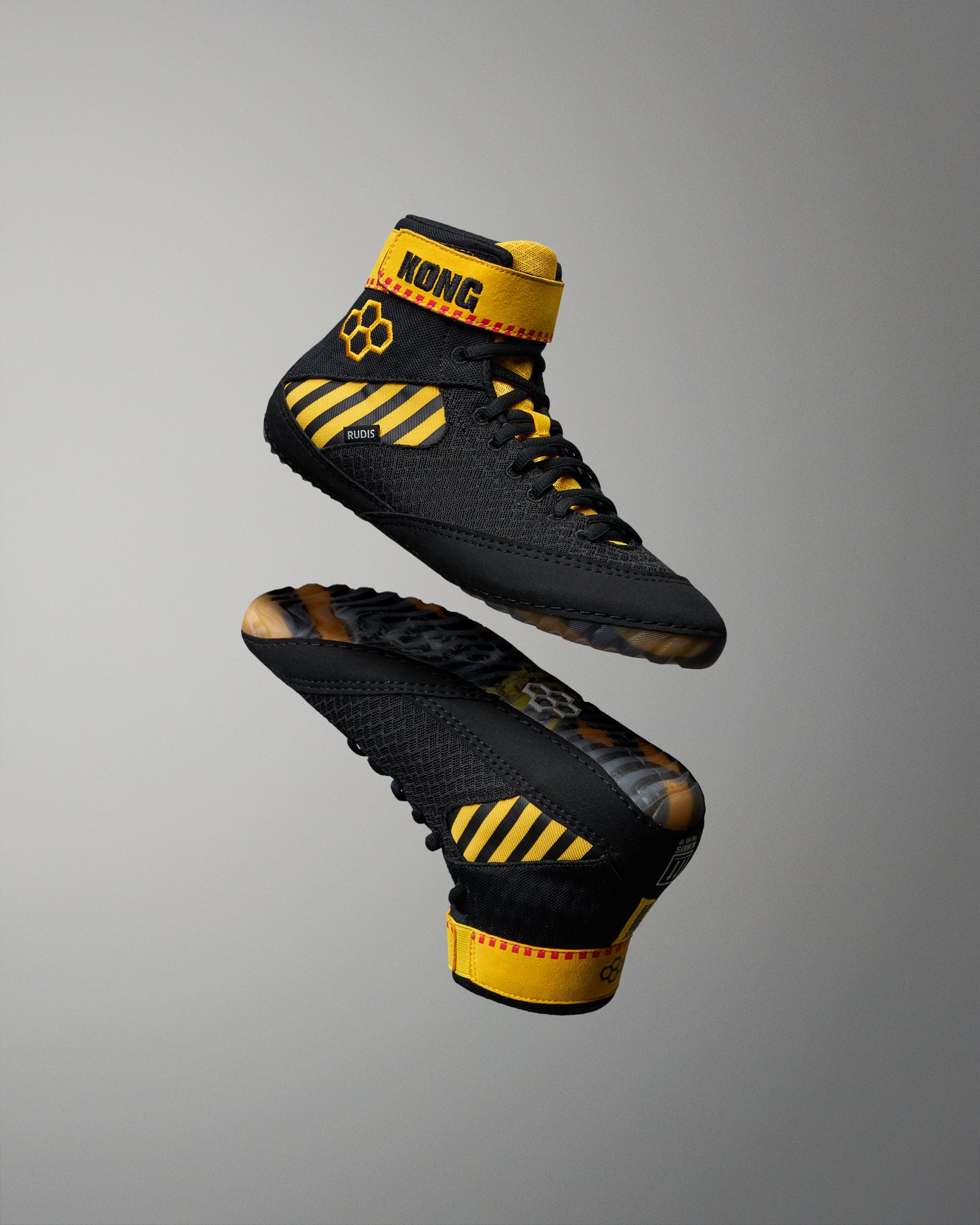 Black high-top wrestling shoes with bold yellow accents and the brand name KONG visible on the ankle strap, shown floating against a smooth gray gradient background.