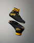 Black high-top wrestling shoes with bold yellow accents and the brand name KONG visible on the ankle strap, shown floating against a smooth gray gradient background.