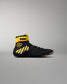 A black high-top wrestling shoe with bright yellow accents, including a yellow ankle strap labeled 'KONG' and yellow diagonal stripes on the side, shown against a neutral gray background.