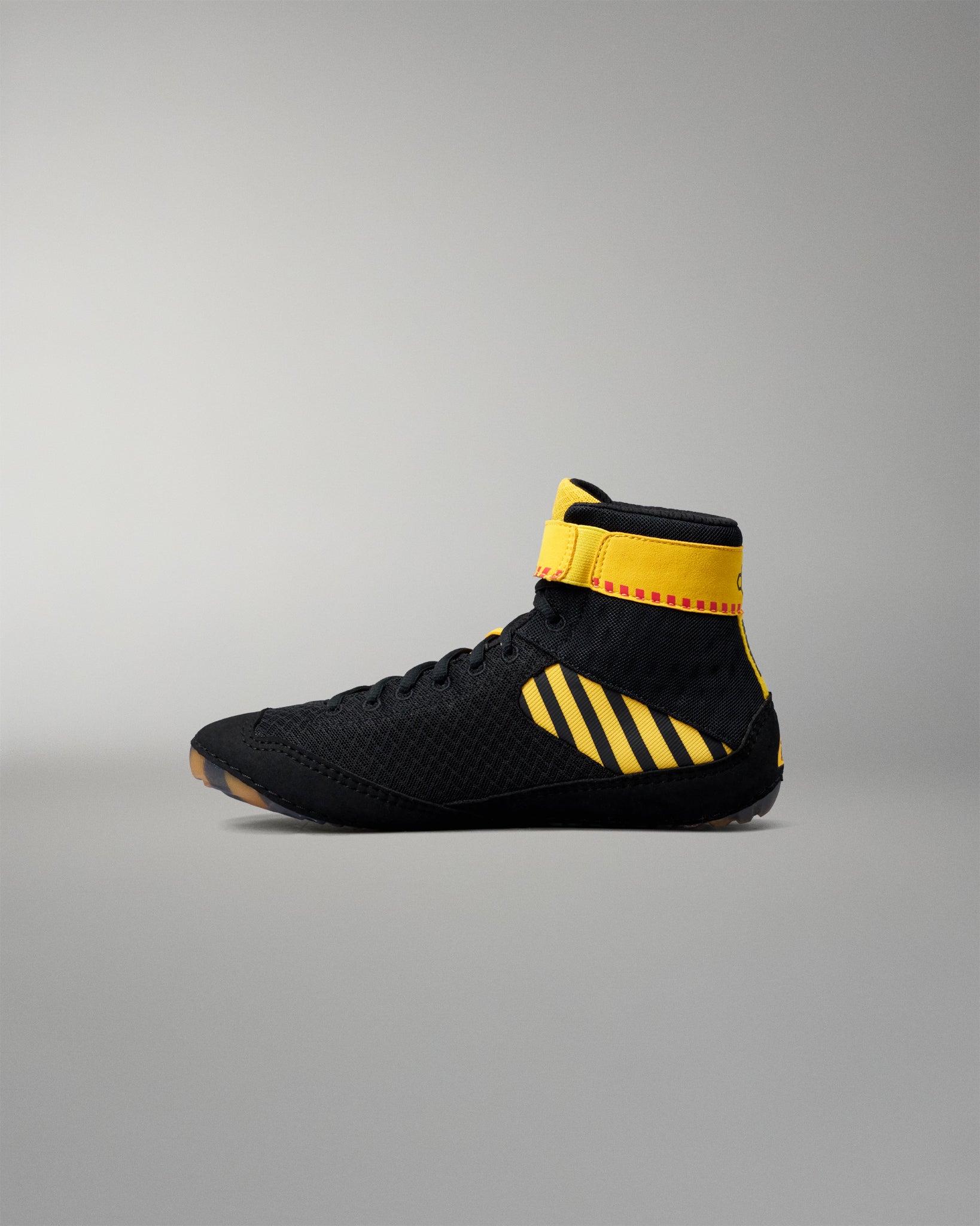 A black high-top wrestling shoe with bold yellow accents, including three diagonal stripes on the side and a yellow ankle strap, shown in profile against a neutral gray background.