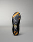 The outsole of a black wrestling shoe with yellow and gray patterned tread, featuring a small white geometric logo near the heel, shown against a neutral gray background.