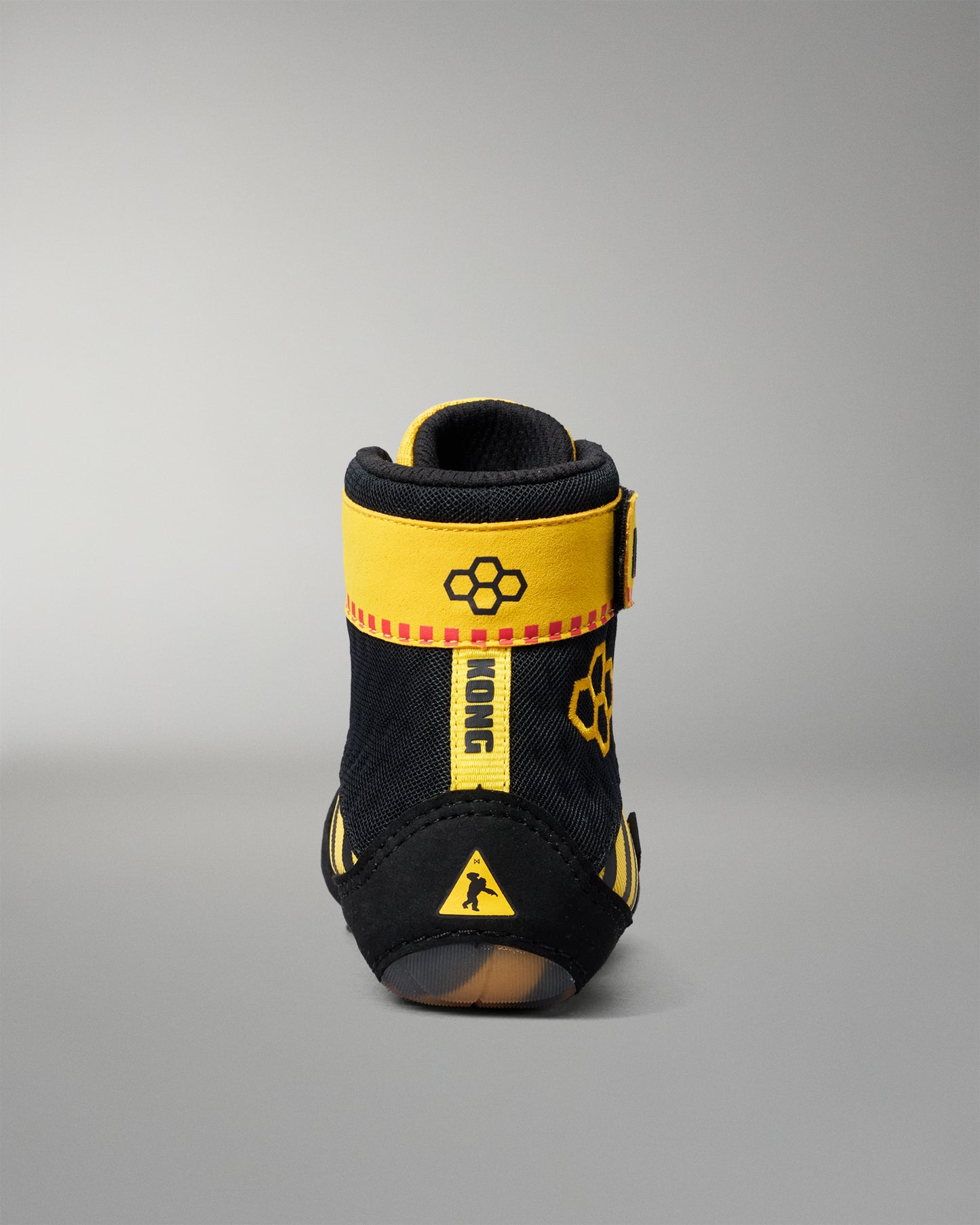 A single black and yellow wrestling shoe shown from the back on a neutral gray background.