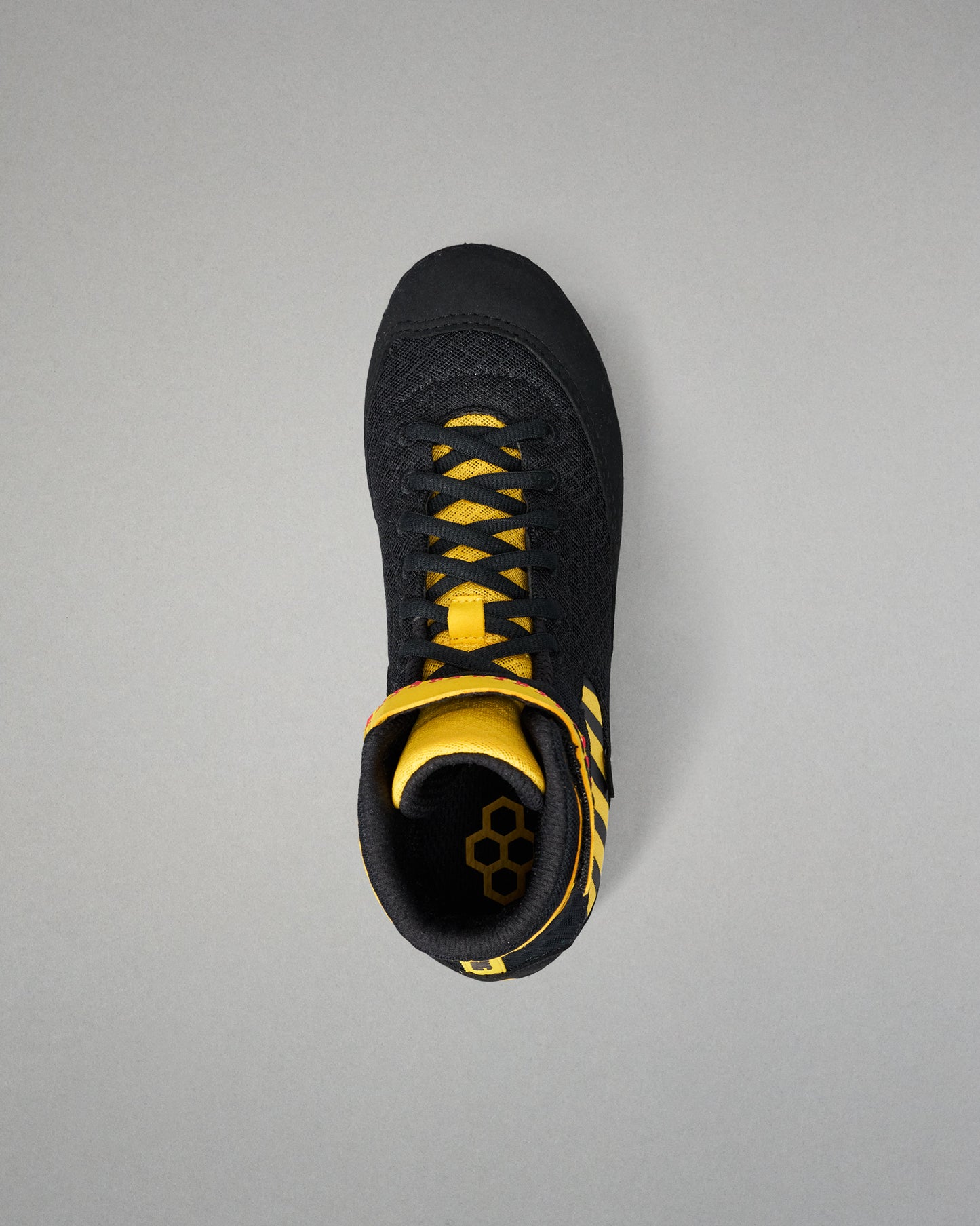 A black wrestling shoe with bright yellow accents, including the laces, collar lining, and side stripes, shown from a top-down view on a neutral gray background.