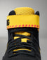 Close-up of a high-top wrestling shoe in black and bright yellow, showing the ankle strap with red stitching and black lettering, black laces, and a textured yellow collar on a gray background.