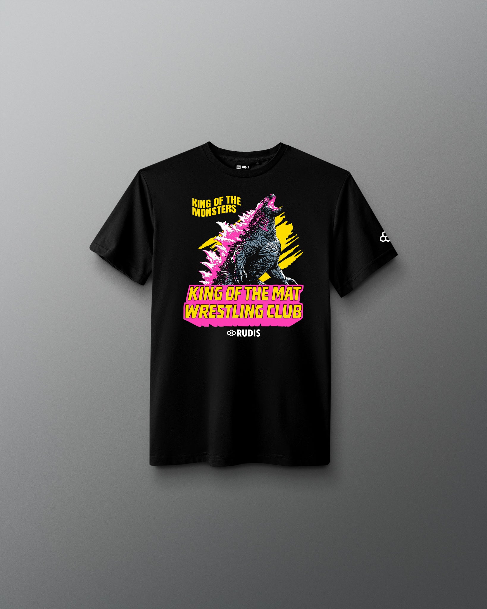 A black short-sleeve graphic t-shirt displayed flat against a dark gray gradient background. The shirt features a colorful front print of Godzilla with the text 'King of the Mat Wrestling Club' in yellow and pink, and a small white logo on the right sleeve.