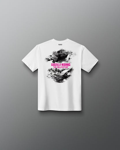 A white short-sleeve t-shirt shown from the back, featuring a black and gray splattered graphic with pink text reading 'Godzilla KONG' and smaller text below, displayed against a dark gray gradient background.