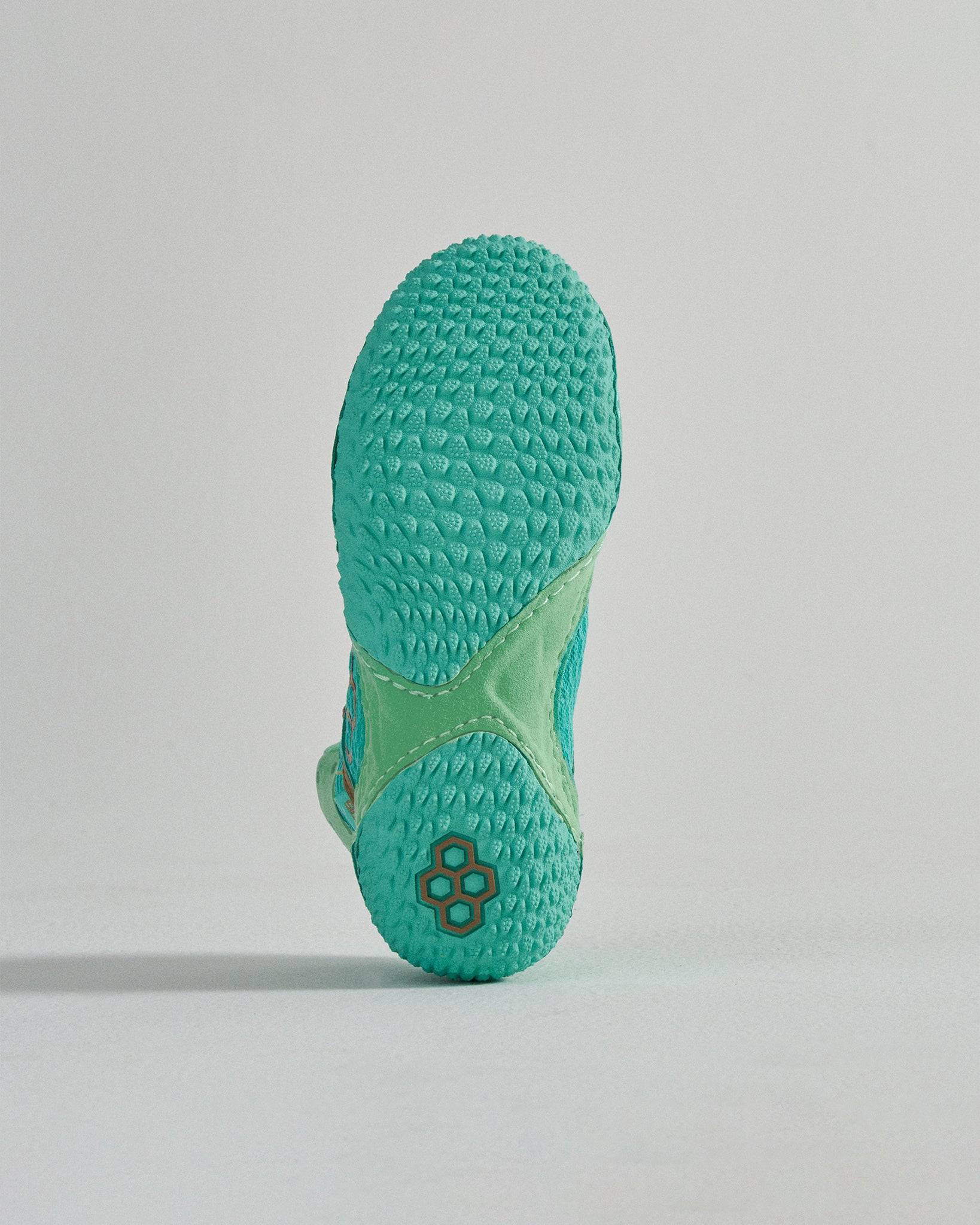 A close-up view of the textured sole of a vibrant turquoise athletic shoe showcasing its unique grip design and color contrast with a light green midsole