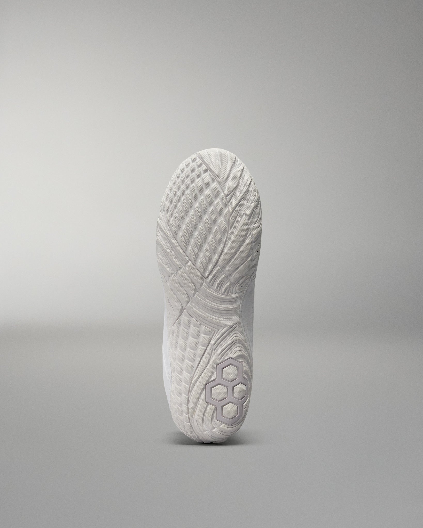 The outsole of a white athletic shoe showcases intricate patterns for traction, highlighted against a light gray background.